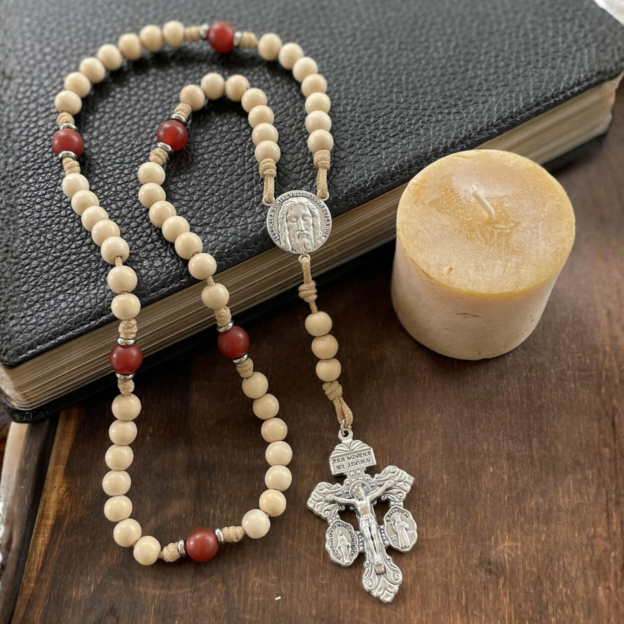 A handmade Seven Sorrows Rosary made from paracord with a silver Pardon Crucifix and silver Holy Face of Jesus centerpiece and the Hail Mary beads are cream color wood and the Our Father beads are red stone.