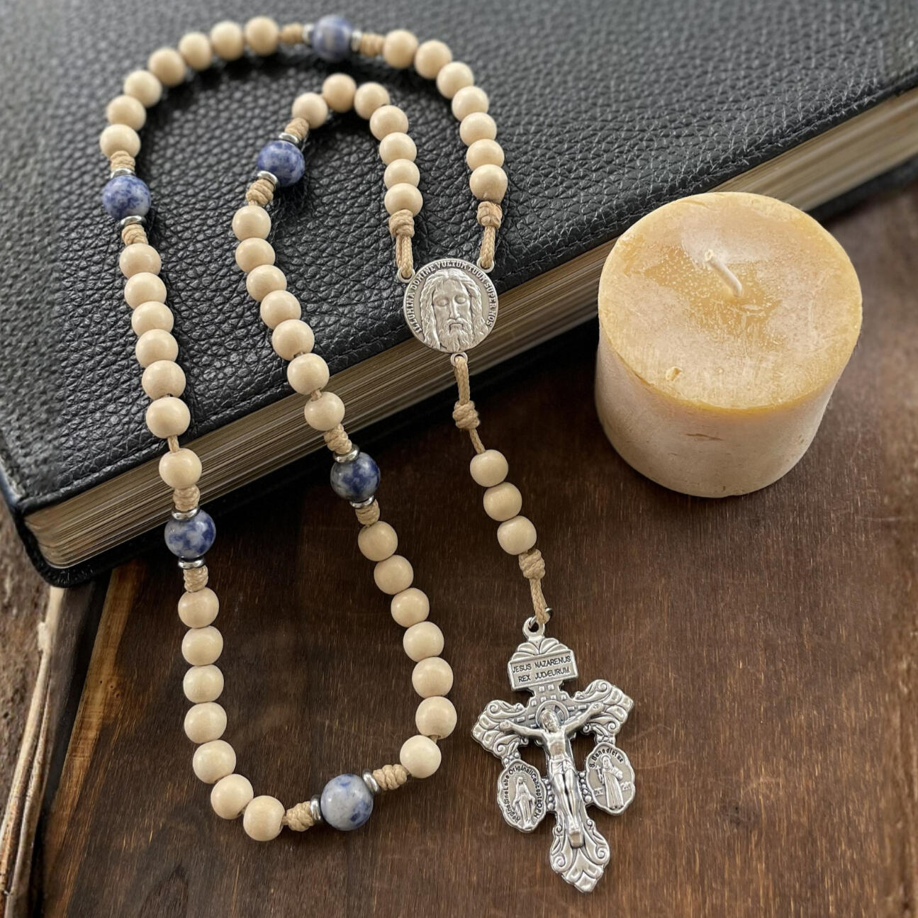 A handmade Seven Sorrows Rosary made from paracord with a silver Pardon Crucifix and silver Holy Face of Jesus centerpiece and the Hail Mary beads are cream color wood and the Our Father beads are blue stone.